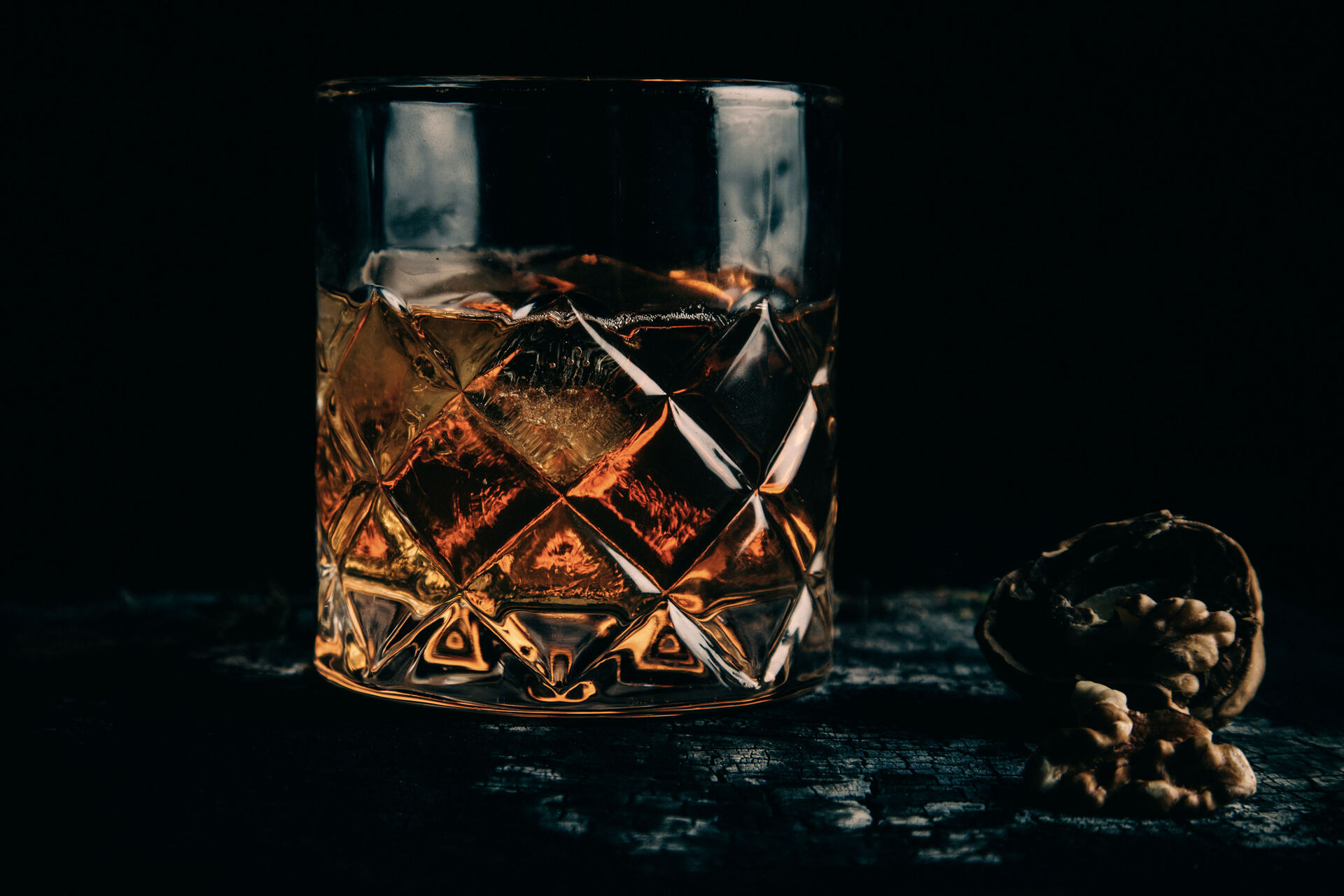 Old fashioned cocktail in low light, deep shadows, amber tones — moody bar atmosphere